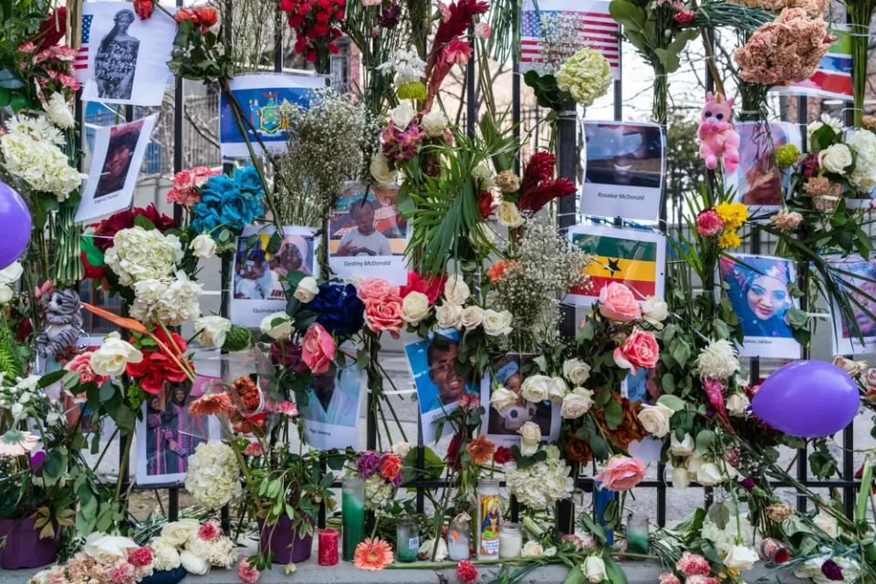 Close-up of fence covered with flowers, flyers, and other memorial items at site of deadly Twin Parks building fire